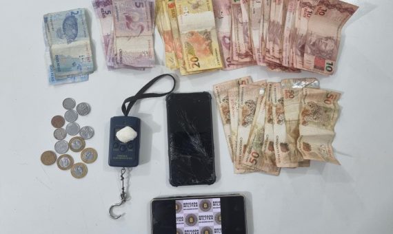 foto colorida de dinheiro, celular e drogas apreendidas em mesa branca