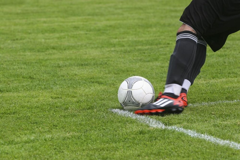 Foto colorida de perna de jogador de futebol realizando chute na bola no gramado
